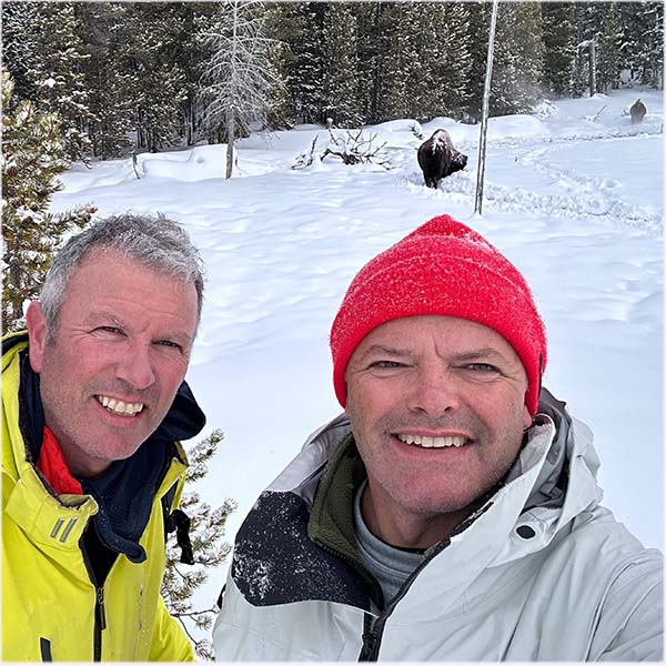 OldFaithfulWinterBisonSelfie Guides of Jackson Hole A selfie of two men in Yellowstone with bull bison in the snow behind them